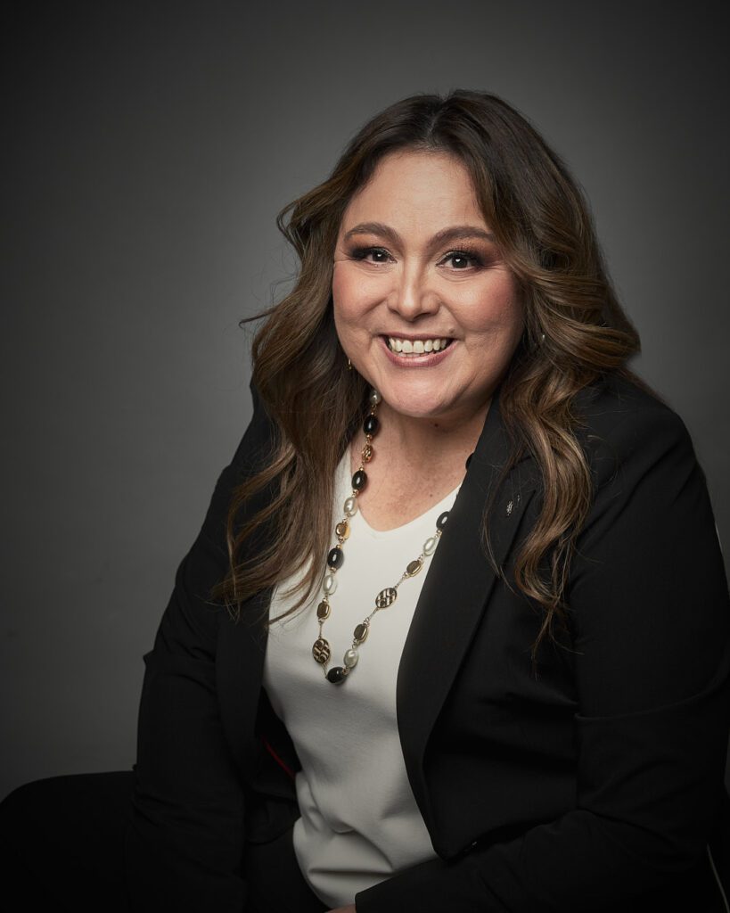 Mujer sonriendo de cabello largo con blusa blanca y saco negro