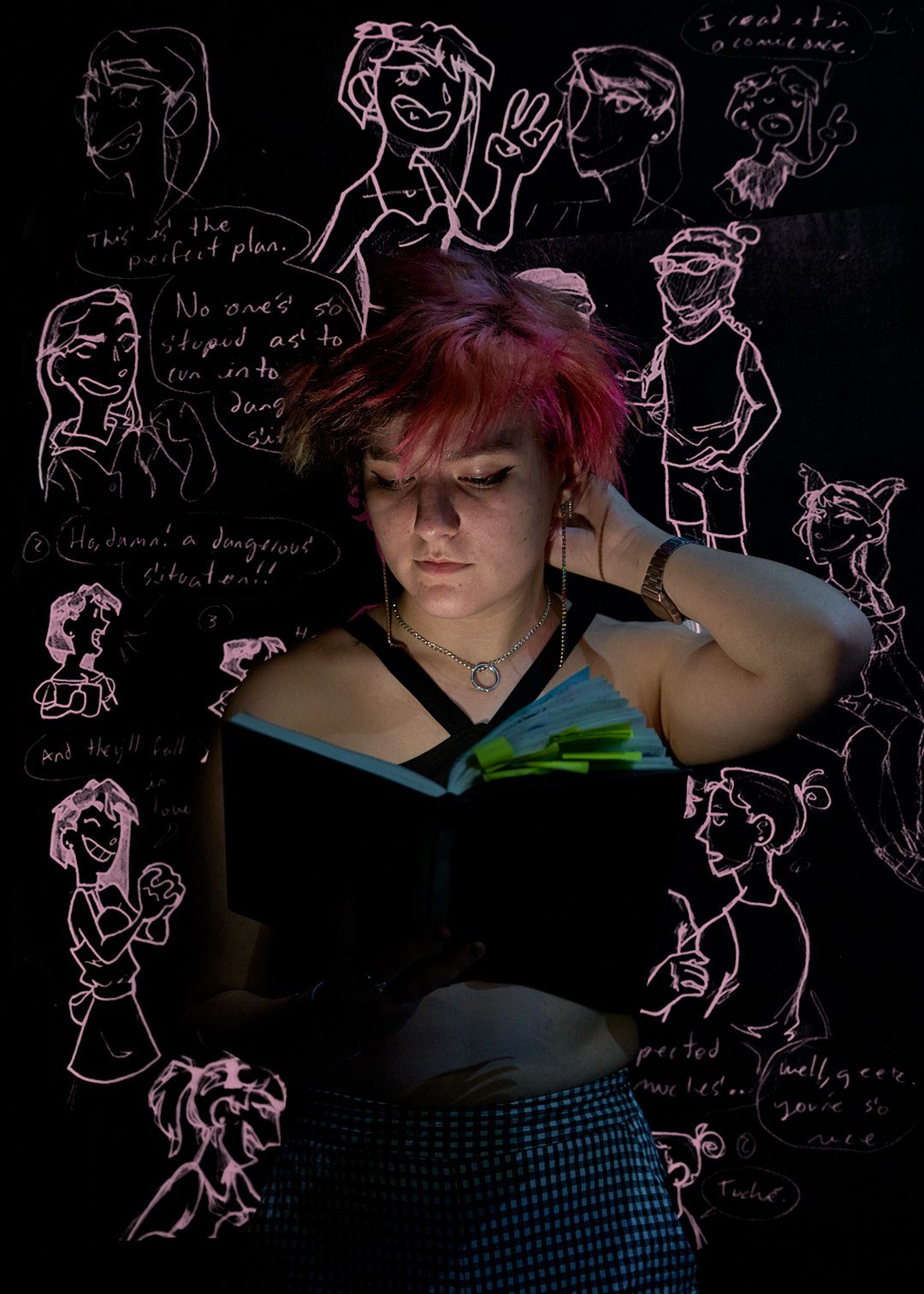 Joven de cabello rosa leyendo libro con dibujos al fondo