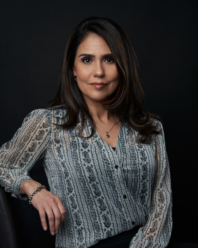 Mujer emprendedora con blusa gris sentada y recargada con su antebrazo sobre el respaldo de la silla