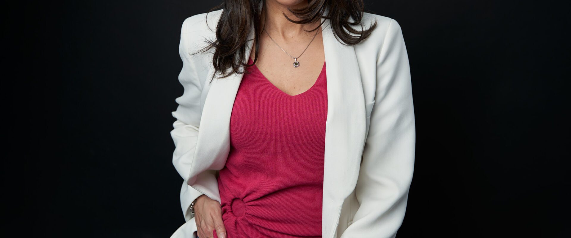 Mujer ejecutiva con blusa rosa y saco blanco parada con la mano derecha en su bolsillo