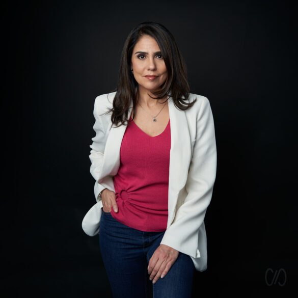 Mujer ejecutiva con blusa rosa y saco blanco parada con la mano derecha en su bolsillo