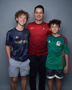 Fotografía de papá y sus dos hijos vistiendo playeras de equipos de soccer