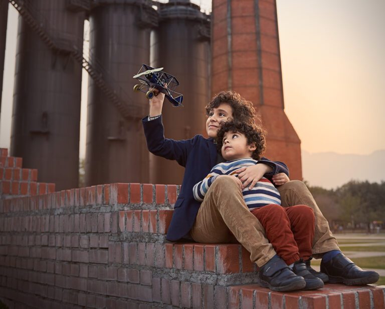 Dos hermanos abrazados jugando con un avión y de fondo una fábrica