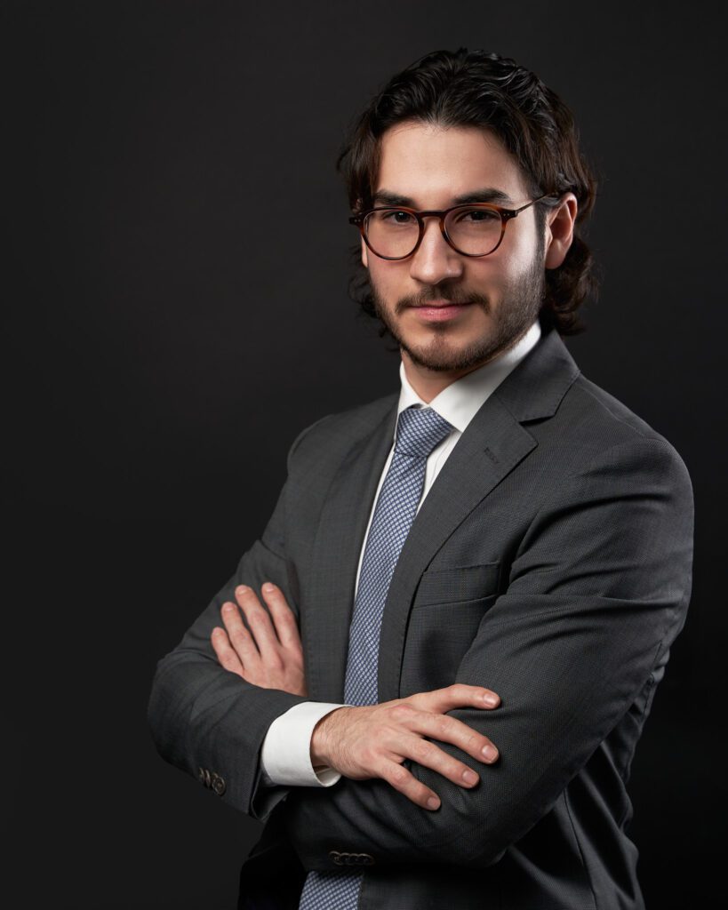 Retrato para LinkedIn de Joven con lentes y traje con corbata azul cruzado de brazos