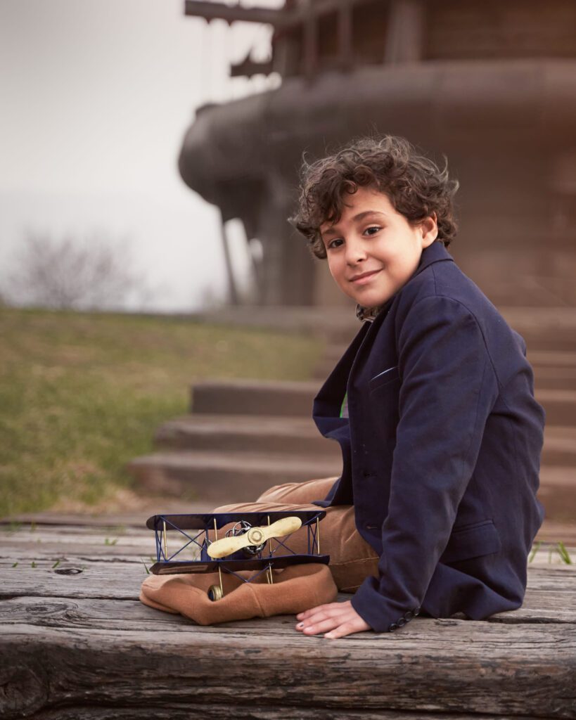 Niño con saco azul sentado con un avión de metal sobre una boina color beige