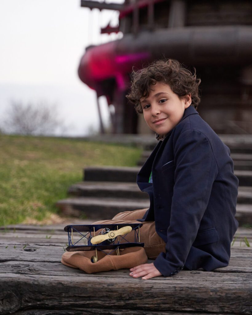 Niño con saco azul sentado con un avión de metal sobre una boina color beige