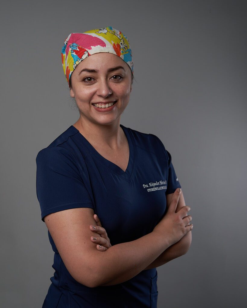 Doctora con gorro de cirugía con sus brazos cruzados y el mentón paralelo al suelo y su mirada a la cámara