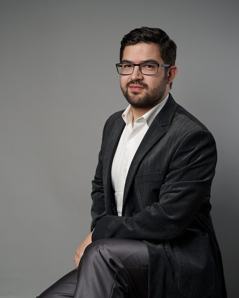 Retrato de cuerpo entero de hombre joven en pose casual con amplia sonrisa  y brazos cruzados, mirando hacia atrás