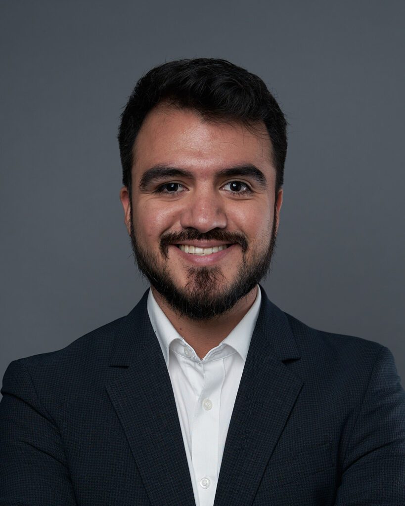 Hombre con barba y con camisa blanca y saco sin corbata con expresión sonriente.