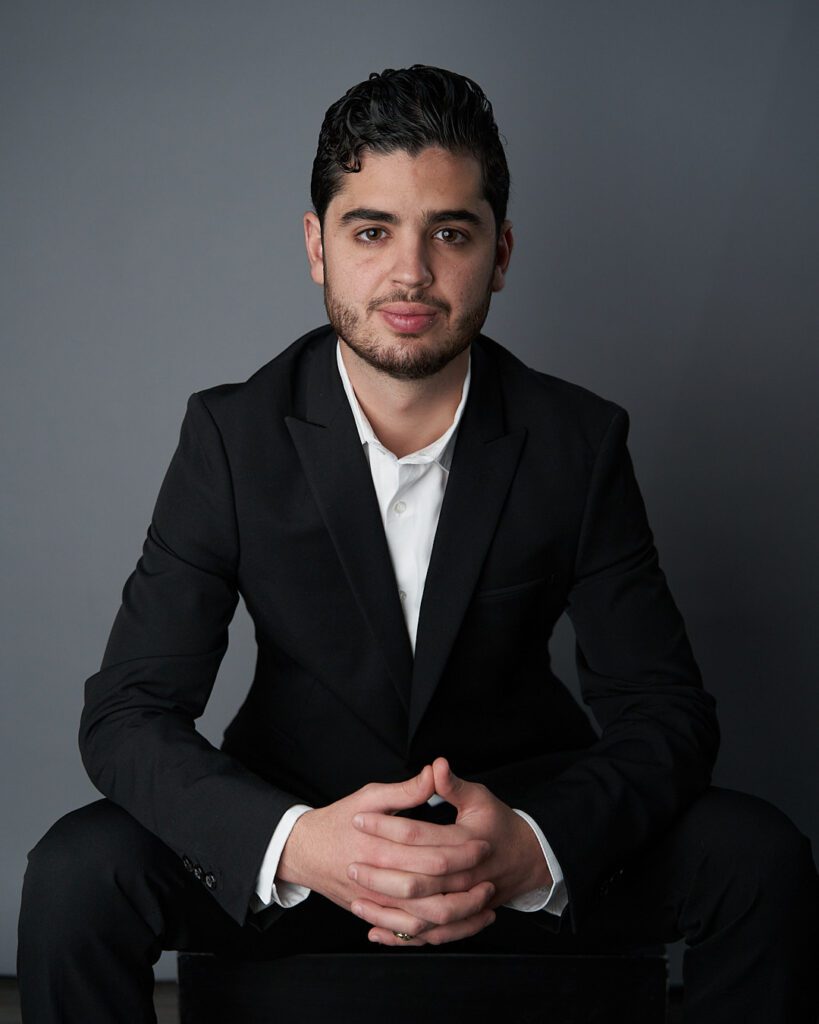 Retrato de cuerpo entero de hombre joven en pose casual con amplia sonrisa  y brazos cruzados, mirando hacia atrás