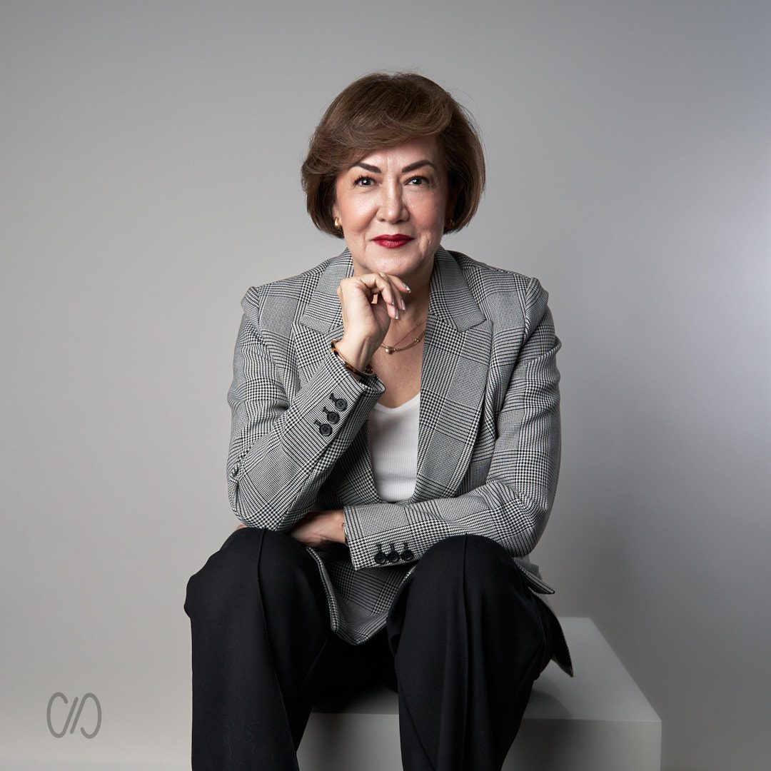 Mujer ejecutiva de 60 años sentada con saco gris y recargada en su rodilla con su codo y apoyando la cabeza en su mano, foto que ayuda a Cómo Ganar Autoridad en LinkedIn